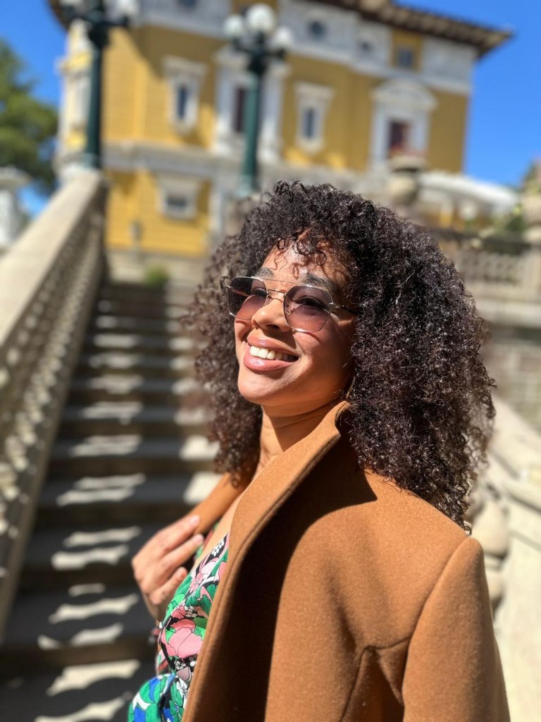Marianela Rosabal sonriendo en escalinata con abrigo camel