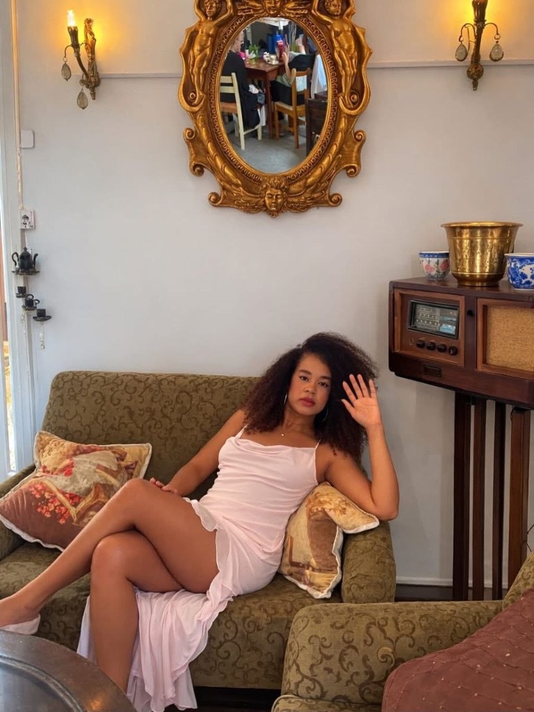 Marianela Rosabal — retrato en vestido rosa sobre sofá vintage
